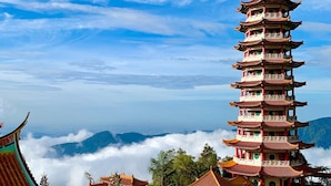 A multi-tiered pagoda with traditional architecture, surrounded by lush greenery and mountains in the background.