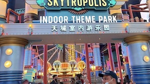 The entrance to the SkyTropolis Indoor Theme Park, featuring a large sign with the park's name and a Ferris wheel in the background.