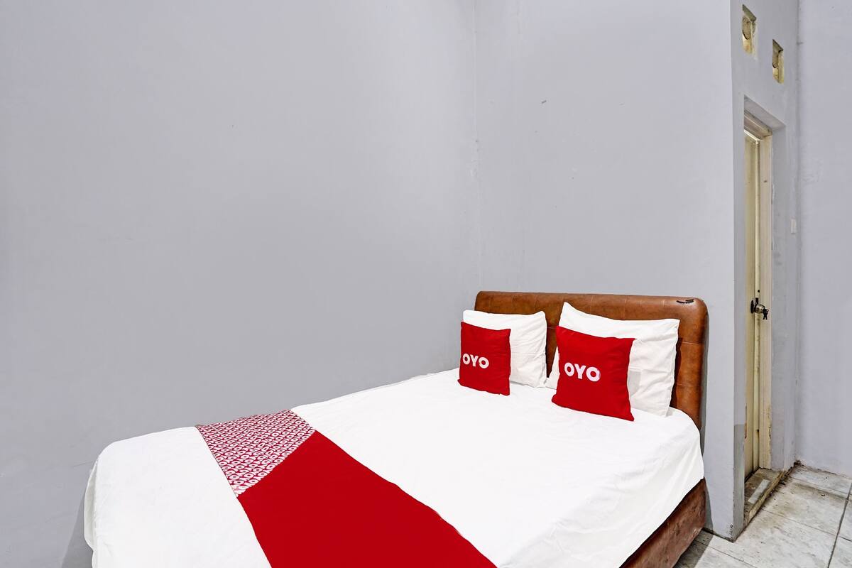 Ein Bett mit weißer und roter Bettdecke, zwei rote Kopfkissen mit dem Schriftzug "OYO" und ein Holz-Kopfteil.