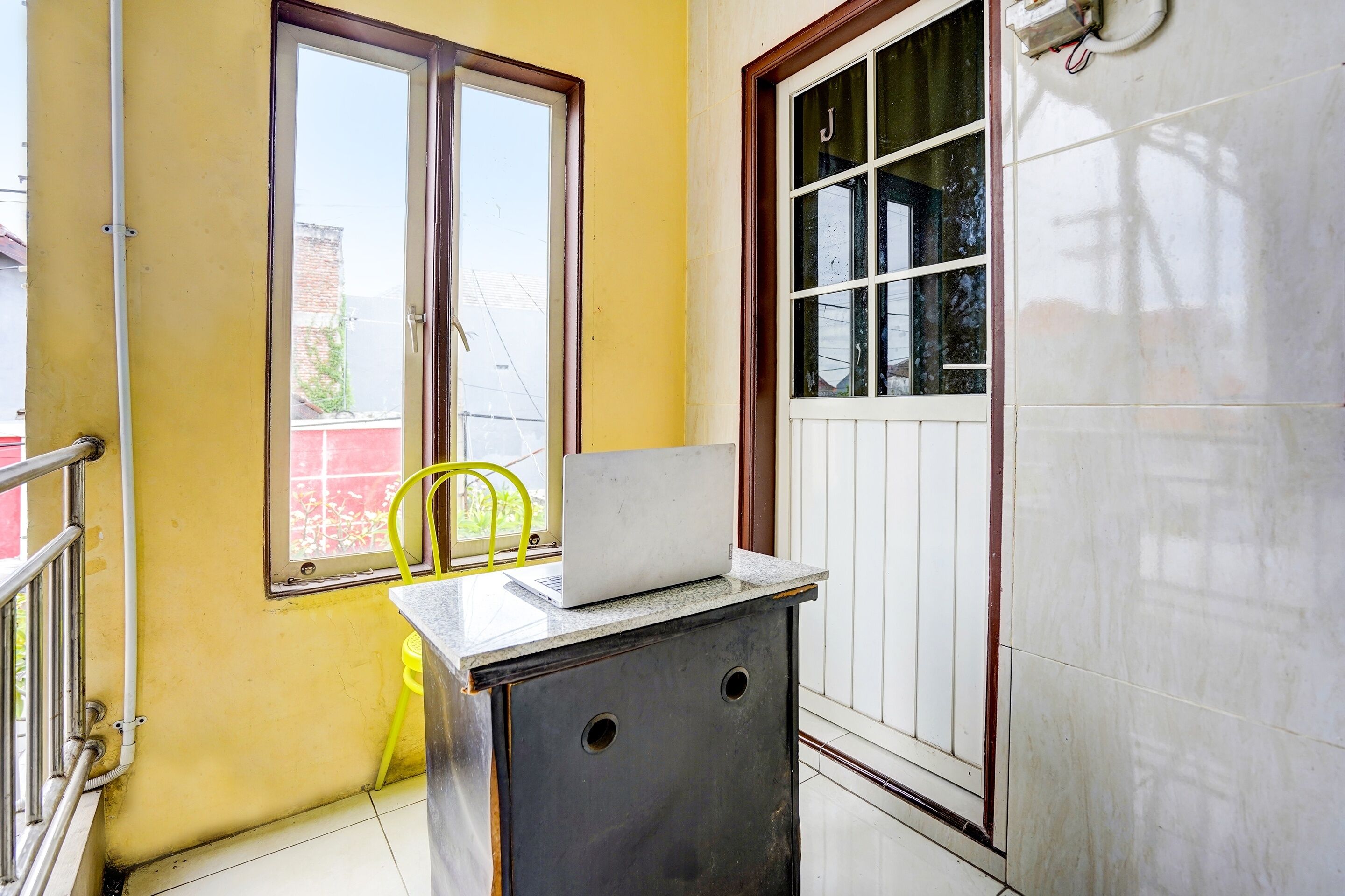 Une petite pièce avec un mur jaune, une fenêtre, une porte et un ordinateur portable posé sur une table.