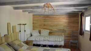 Ein Schlafzimmer mit einem Holzkopfteil, einem Bett mit einer Steppdecke, einem Sessel und einer Hängeleuchte.