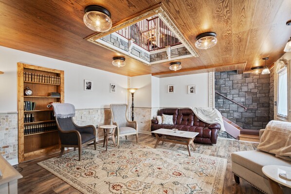 A spacious living room with a high ceiling, a fireplace, a staircase, and a wooden bookshelf. - Two master suites in historic downtown (Luray)