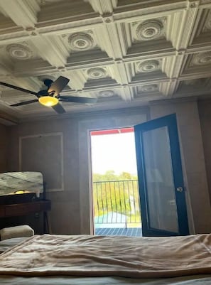 Una habitación con cama, ventilador de techo y puerta que da a un balcón al aire libre.