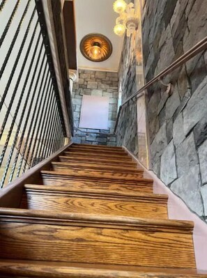 A wooden staircase with a stone wall on one side and a metal railing on the other. - Two master suites in historic downtown (Luray)