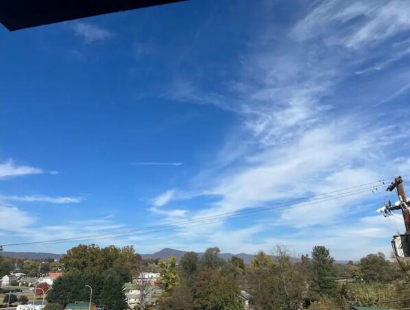 A clear blue sky with scattered clouds, a mountainous landscape in the distance, and a residential area with houses and trees. - Two master suites in historic downtown (Luray)