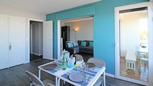 A dining area with a table set for four, a sofa in the background, and a sliding glass door leading to an outdoor seating area. - L'abricôtier - Arcachon (ARCACHON)