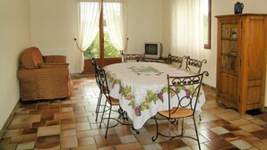 Zona pranzo con tavolo rotondo, sedie, televisore e un armadio.