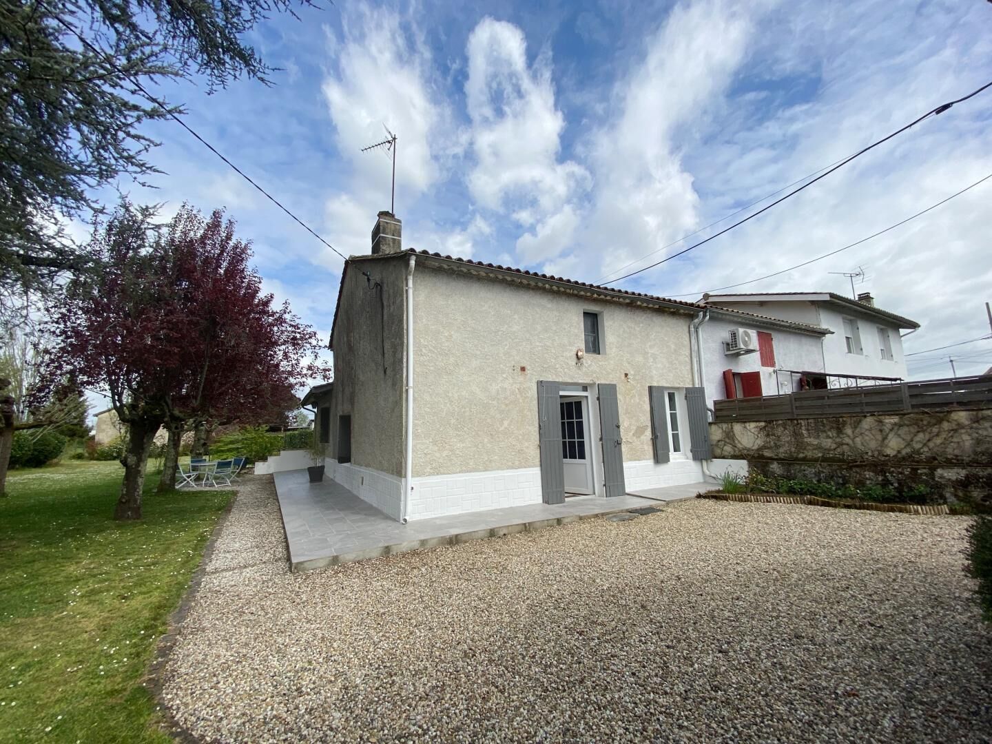 Un bâtiment à deux étages avec une allée gravillonnée, un petit jardin et un arbre aux feuilles rouges.