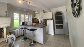 Une cuisine moderne avec un îlot central, des luminaires suspendus, un réfrigérateur et une horloge au mur.
