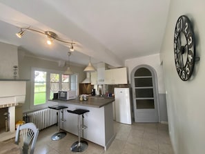 A modern kitchen with a central island, pendant lights, a refrigerator, and a clock on the wall.