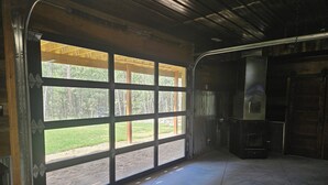 Een garage met een grote open deur, een betonnen vloer en een zichtbaar buitengebied met bomen.
