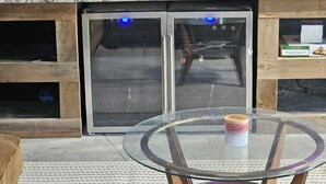 Een glazen tafel met een bak, een barbecuegedeelte met een hor, en een stenen muur.