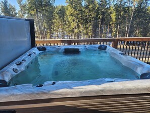 A hot tub with a wooden deck and a view of a forest.