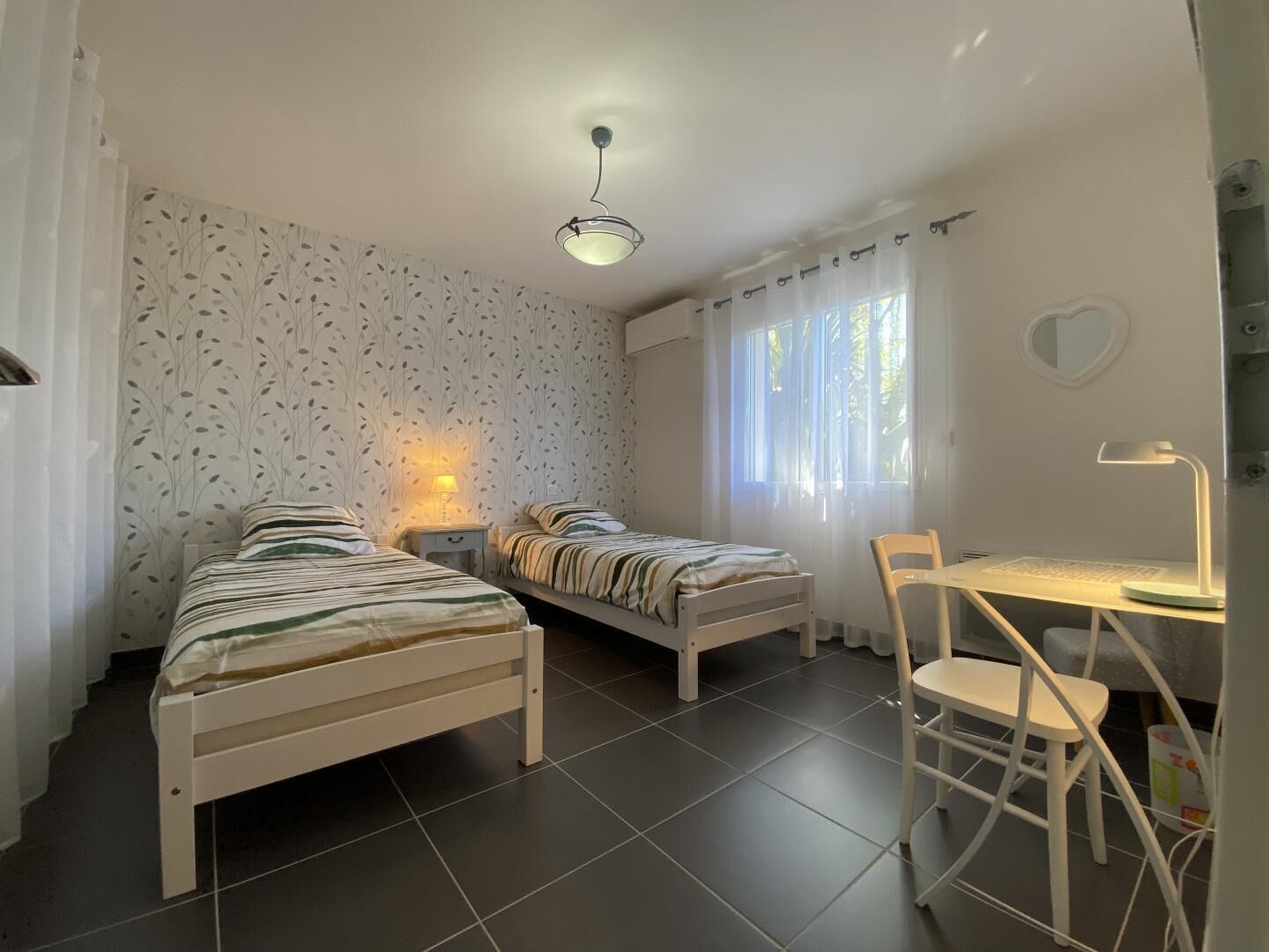 Et værelse med to enkeltsenge, et skrivebord med stol, et lille bord og en loftlampe.