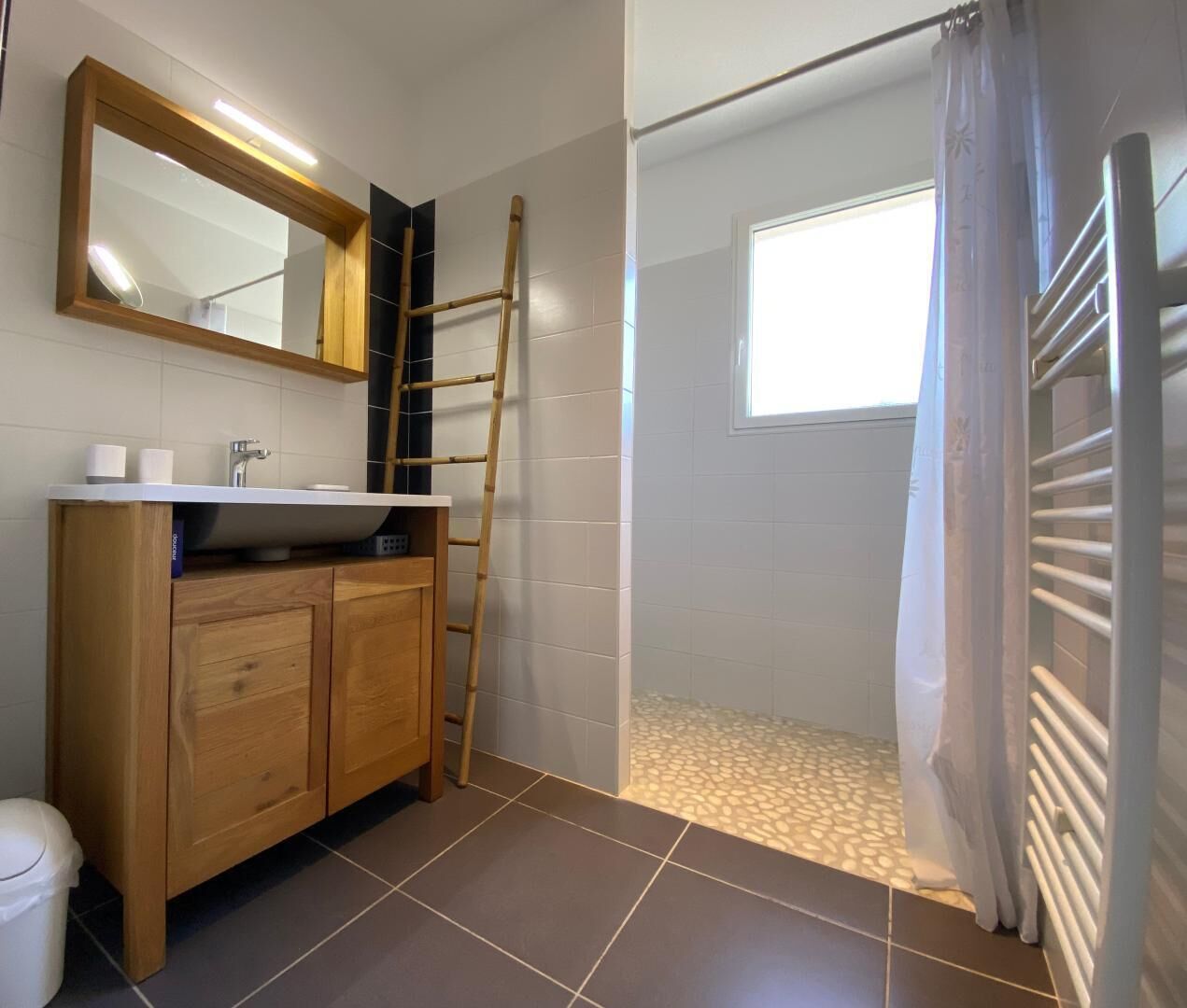 Un baño con tocador de madera, un espejo, ducha con puerta de cristal y ventana que proporciona luz natural.