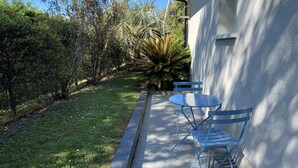 A patio with a table and chairs, a small garden with various plants, and a building in the background. - Aux Lauriers Roses - Hourtin (HOURTIN)