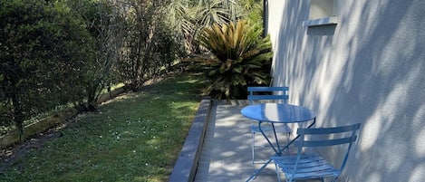 Une terrasse avec une table et des chaises, un petit jardin avec différentes plantes et un bâtiment en arrière-plan.