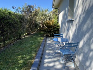 Un patio con tavolo e sedie, un piccolo giardino con diverse piante, e un edificio sullo sfondo.