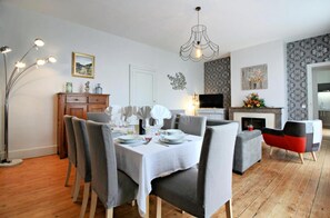Un comedor con una mesa dispuesta para cuatro, una lámpara moderna y una chimenea con un ornamentado hogar.