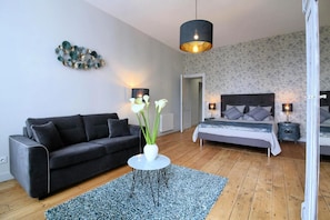 Una sala de estar moderna con un sofá negro, un jarrón blanco con flores, una mesa redonda de centro y una alfombra azul.