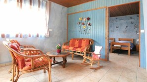 Ein Zimmer mit Rattanmöbeln, einer Couch, einem Schaukelstuhl, einem kleinen Tisch und einem Fenster mit Vorhängen.