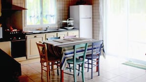 Eine Küche mit Herd, Spüle und Kühlschrank. Ein Esstisch mit Stühlen und ein Fenster mit Vorhängen.