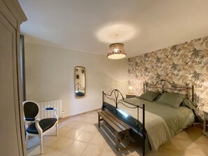 Un dormitorio con cama, una silla, una mesita de noche, un espejo y una lámpara colgante.