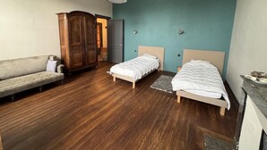 A bedroom with two single beds, a wooden wardrobe, a sofa, and a ceiling light. - Gite DE Micalet - Cussac-fort-medoc (CUSSAC-FORT-MEDOC)
