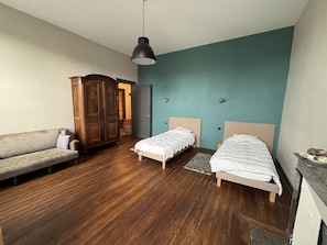 Een slaapkamer met twee eenpersoonsbedden, een houten garderobe, een bank en een plafondlamp.