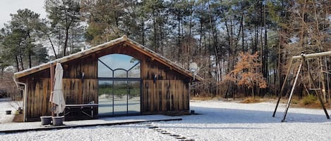 Una cabaña de madera con un gran ventanal, rodeada por un paisaje nevado y árboles.