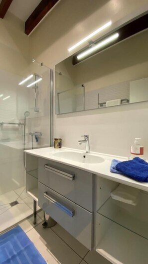 Ein modernes Badezimmer mit Glasdusche, einem Doppelwaschbecken und einem großen Spiegel.