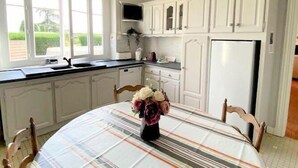 Una cocina con armarios blancos, una mesa de comedor con mantel a rayas y un jarrón con flores.