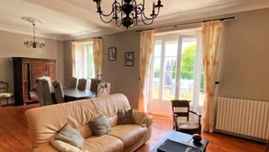 Una sala de estar con sofá de cuero, una mesa de centro, una araña y un comedor con sillas y una mesa.