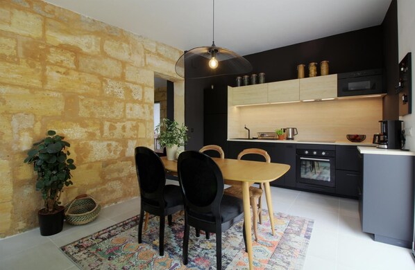 A modern kitchen with black cabinets, a wooden dining table, and a hanging light fixture.