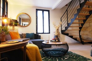 A living room with a sofa, a round coffee table, a lamp, a mirror, a staircase, and a window.