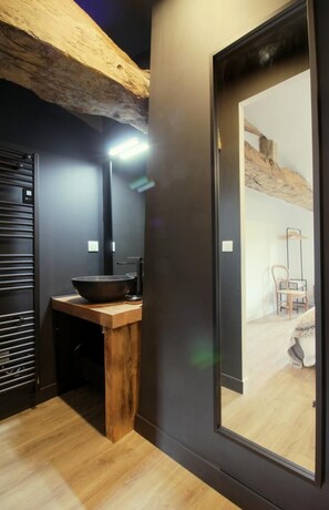 Un baño moderno con tocador de madera, un espejo grande y zona de ducha visible.