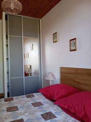 A bedroom with a bed, a wardrobe, a lamp, and two framed pictures on the wall.
