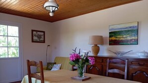 Ein Essbereich mit Tisch für zwei Personen, Stühlen, einer Blumenvase, einer Lampe und einem Gemälde an der Wand.