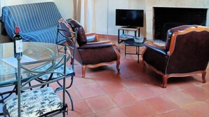 Un soggiorno con un divano, due poltrone, un tavolino in vetro, una televisione, un camino e uno specchio a parete.
