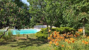 A swimming pool surrounded by lush greenery and flowering plants. - Gîte Les Trois Moulins (MOMBRIER)