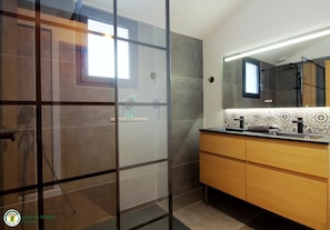 Bathroom features a glass shower enclosure, a vanity with a countertop, and a large mirror.