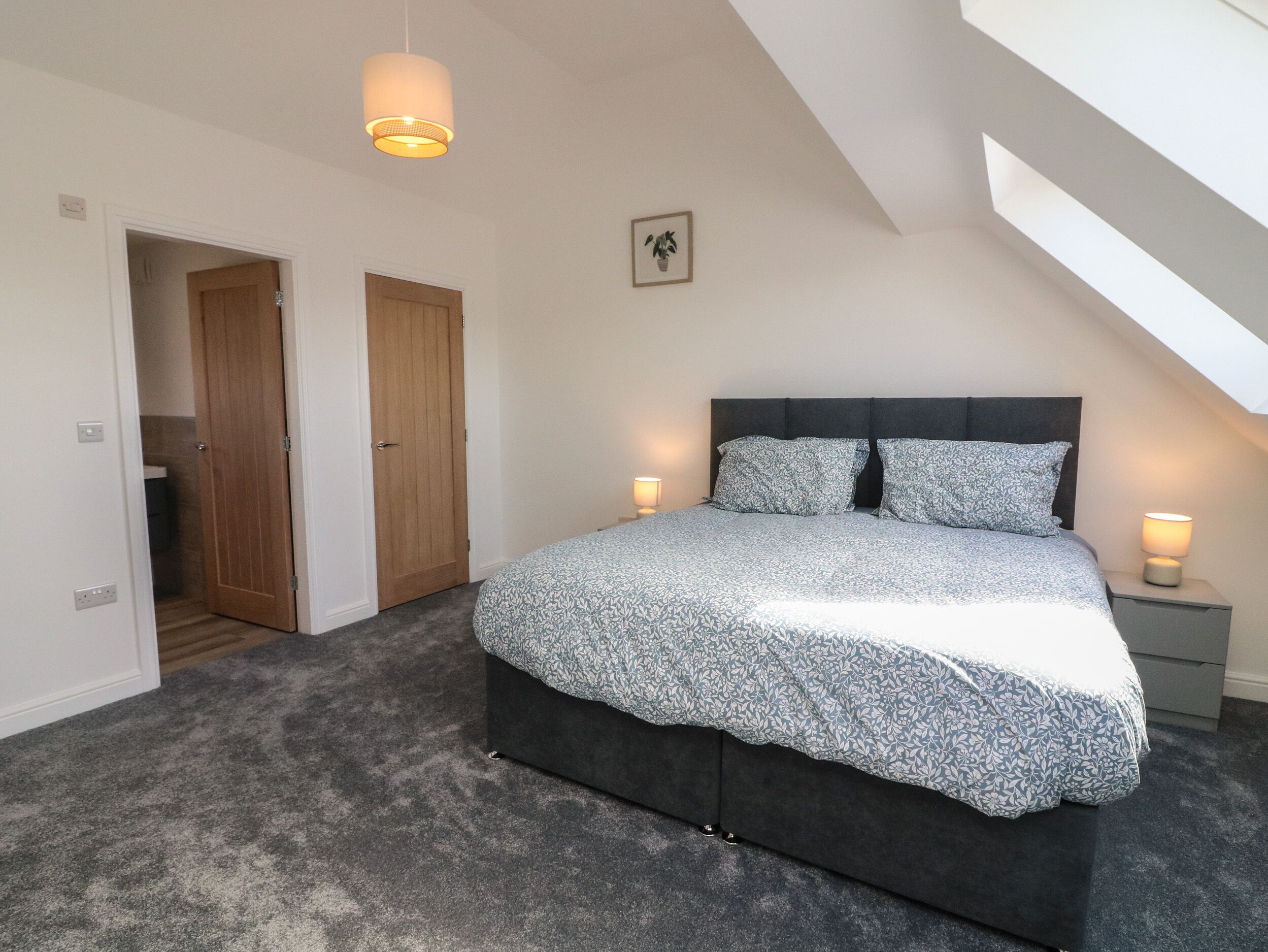 A bedroom with a large bed, two bedside lamps, a ceiling light, a door, and a small picture on the wall.