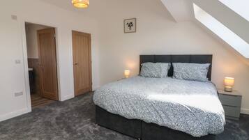 A bedroom with a large bed, two bedside lamps, a ceiling light, a door, and a small picture on the wall.
