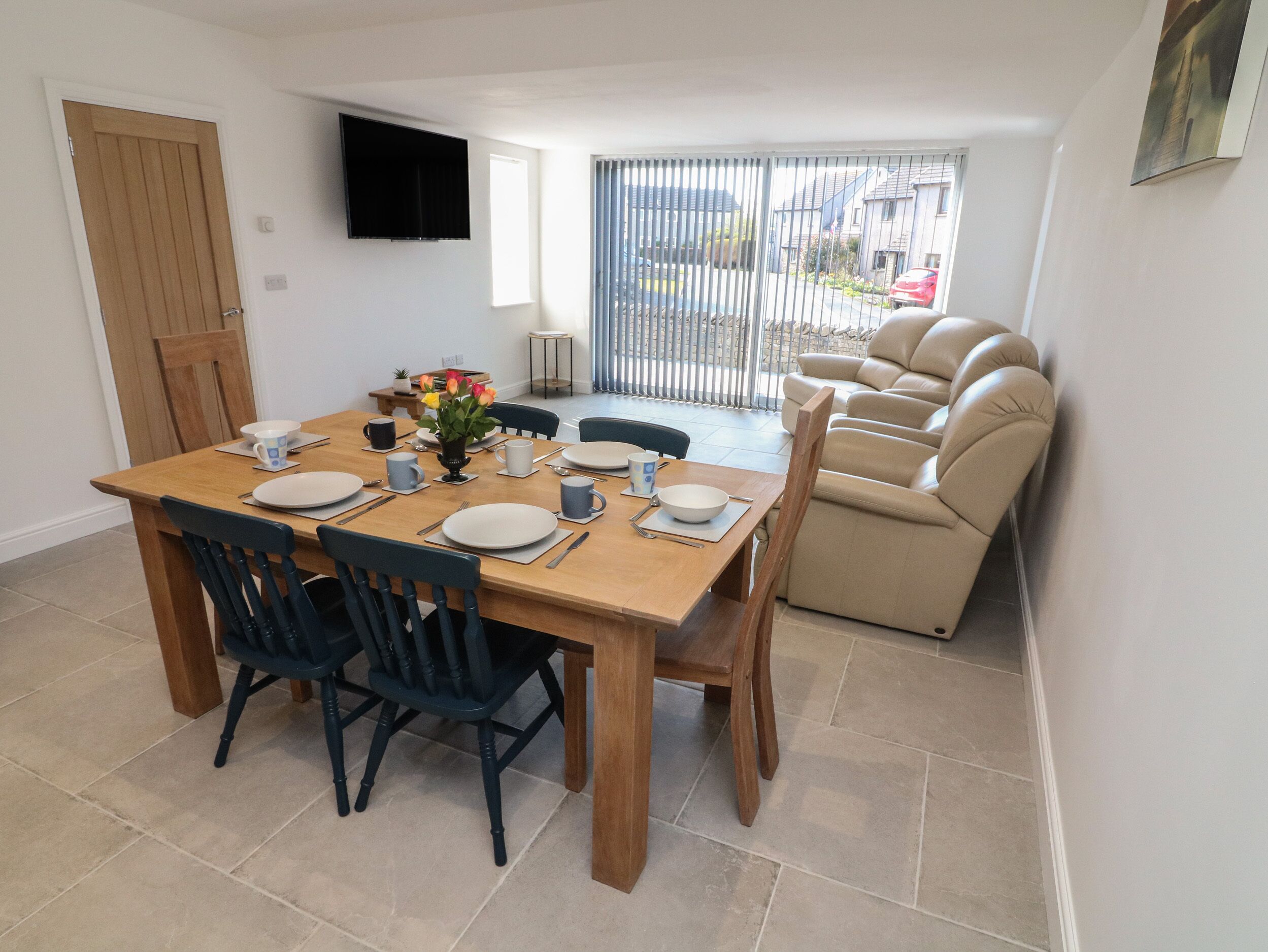 A dining area with a wooden table set for four, surrounded by chairs, and a sofa with a reclining chair.