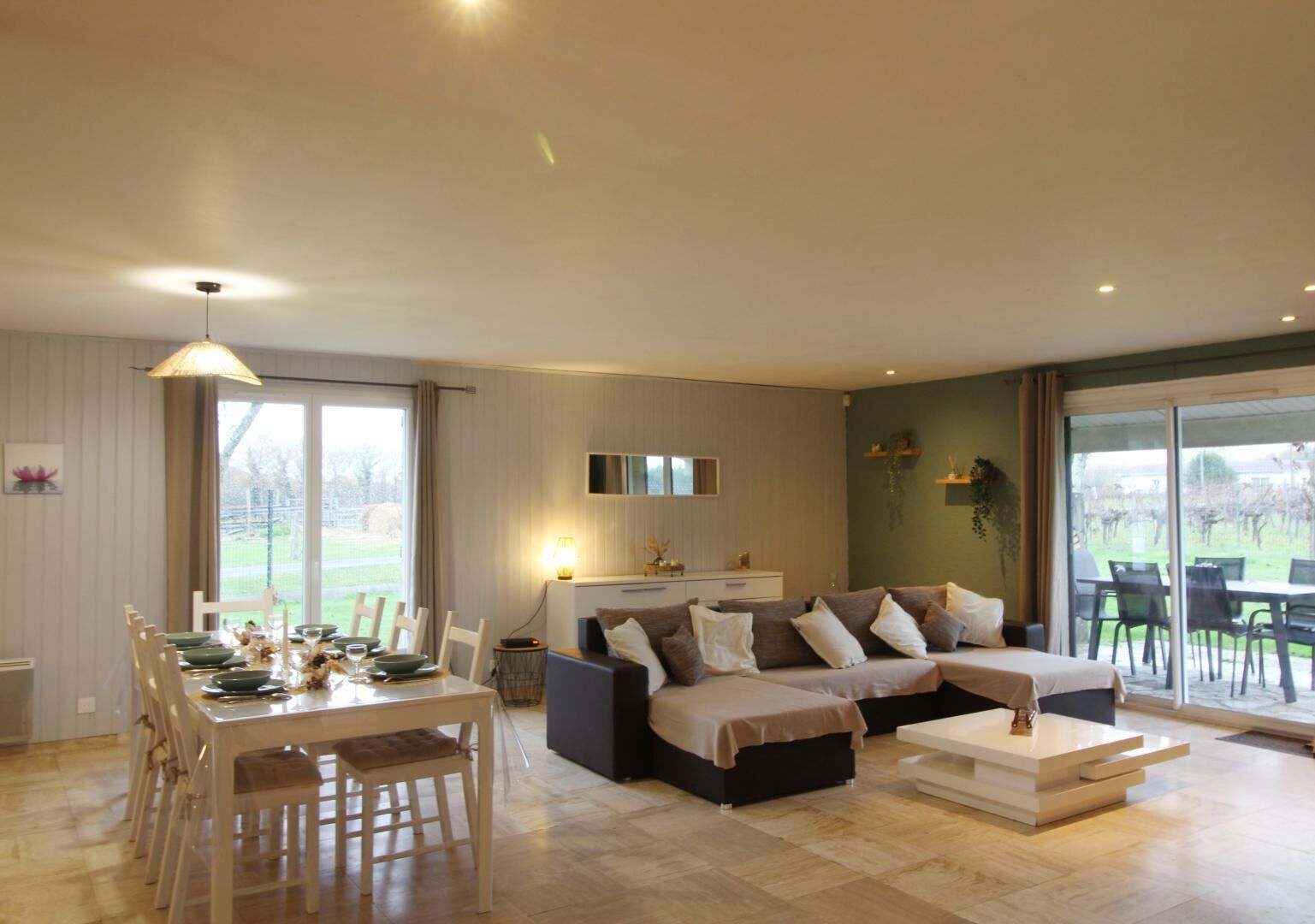Ein modernes Wohnzimmer mit Essbereich, einer Sofagarnitur und einem großen Fenster mit Blick ins Freie.