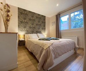 A bedroom with a bed, a nightstand, a lamp, a radiator, and a window with curtains.