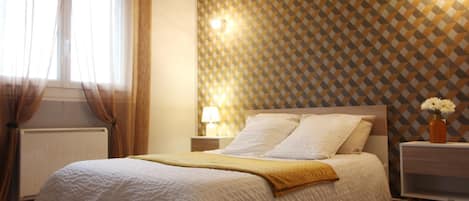 A neatly made bed with a white duvet, a bedside lamp, and a vase with flowers on a nightstand.