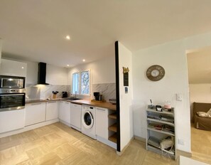 Une cuisine compacte équipée d’un four à micro-ondes, d’un four traditionnel et d’un lave-linge, avec un plan de travail en bois et une fenêtre offrant une vue agréable.