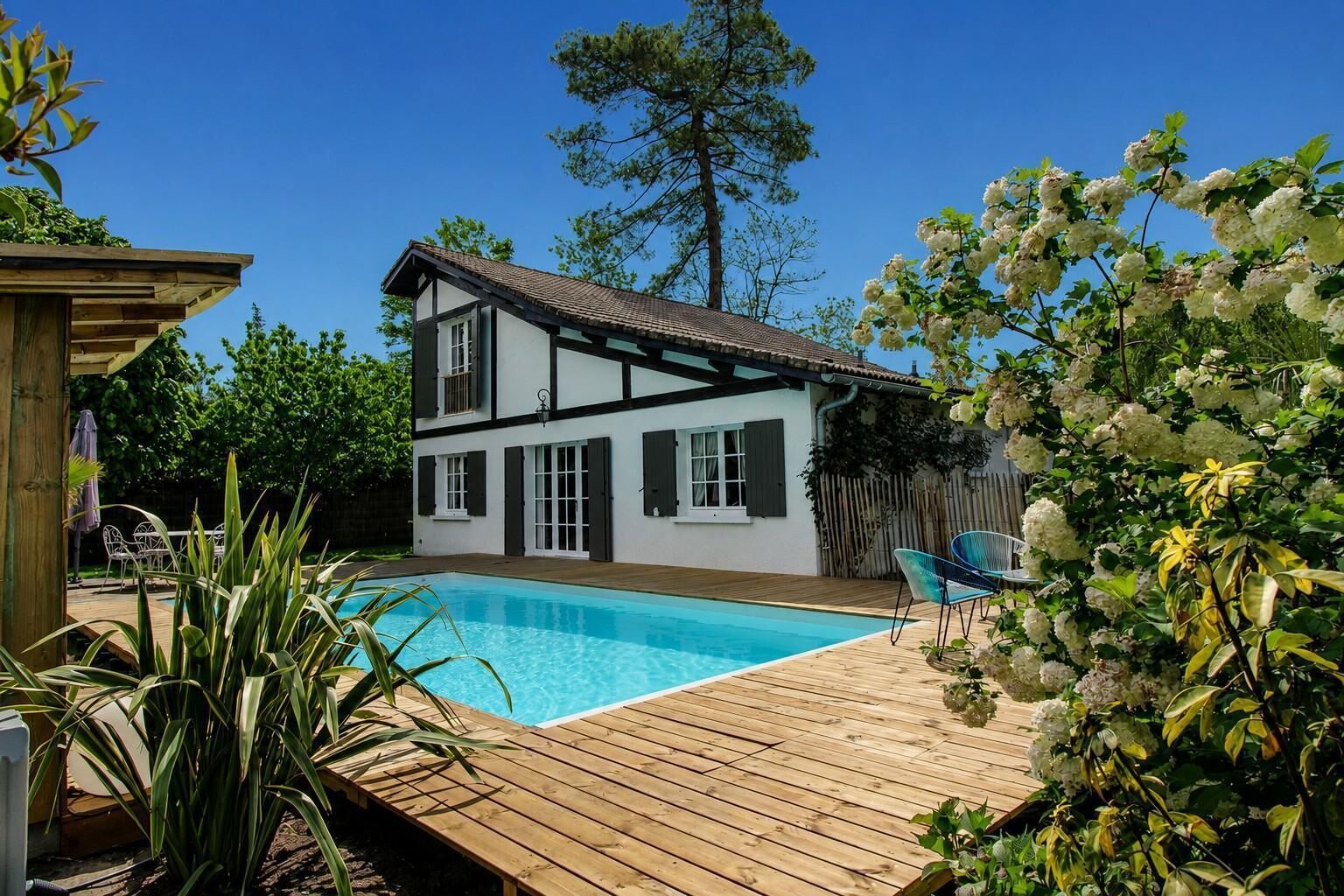 A two-story house with a swimming pool, wooden deck, and outdoor furniture.