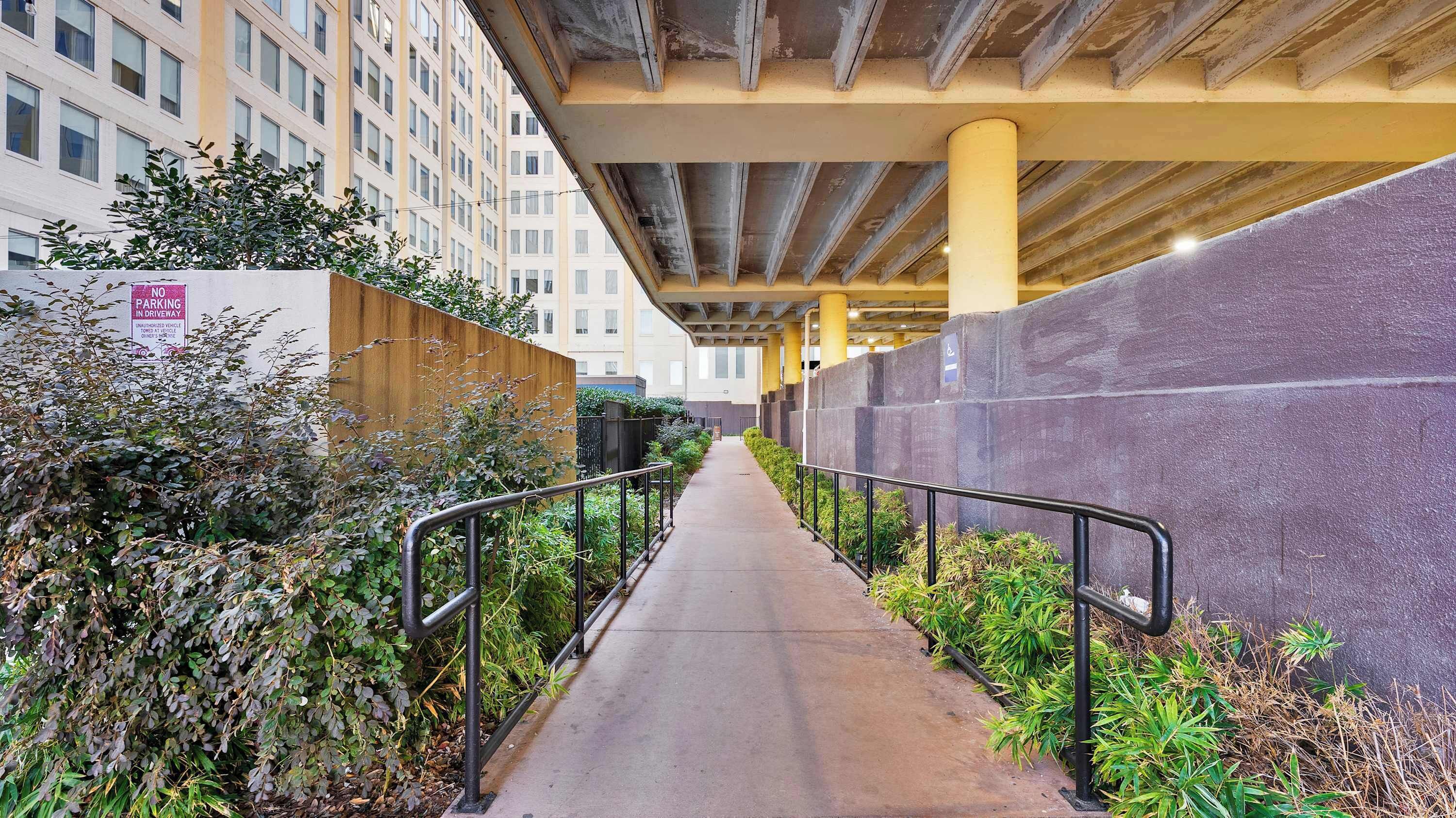 A pedestrian walkway under a bridge with a concrete barrier on one side and a building on the other.